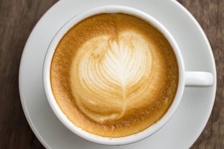 Cup of hot coffee latte with latte art on wooden table