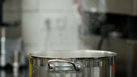 Vapour clouds rising from boiling water in pan on stove. Media. Steam and white smoke rising on professional kitchen background. Steam from pan while cooking. Cooking process in slow motion.の写真素材