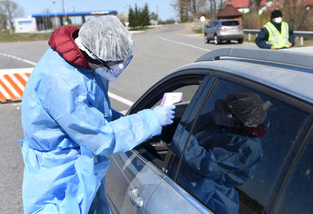 Lviv, Ukraine - April 10, 2020: Medical worker checks temperature of a driver on a checkpoint on the...