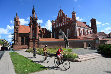 Vilnius, Lithuania - July 22, 2024: A people on bicycles near St. Anne's Church and Church of Saints...