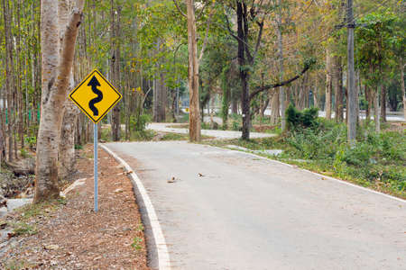 Curves ahead traffic sign. Nature green trees with rural road bike in quiet park in spring.at sunny...