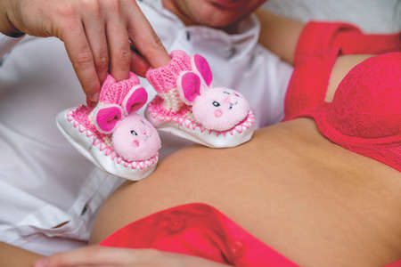 young man touch a pregnant woman stomach with baby shoesの写真素材