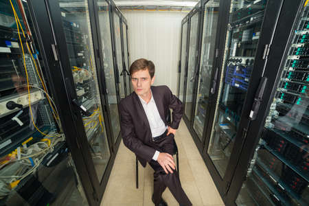 Network Engineer in the server room in a suit sitting on a chair, distorted perspective
