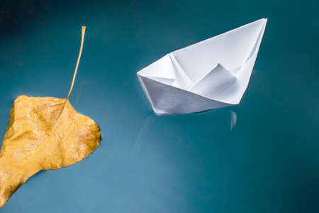 Autumn leaf and a paper boat on the blue water surfaceの写真素材