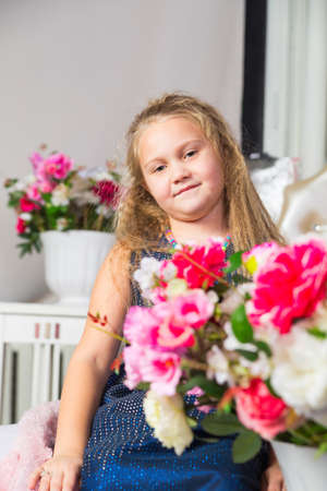 Little girl in a blue dress sitting on the couch in the background flowers, focus on girlの写真素材