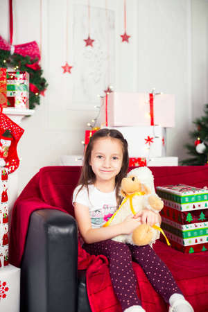Little girl sitting on the coach holding a stuffed toy, Christmas gift, tray in the backgroundの写真素材