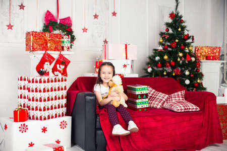 Little girl sitting on the coach holding a stuffed toy, Christmas gift, tray in the backgroundの写真素材