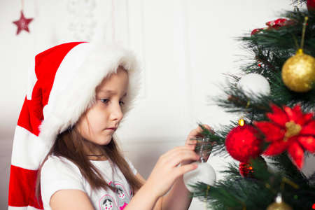 little girl in a red cap hangs on the Christmas tree new year toysの写真素材