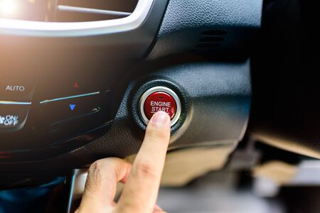 Asian man's finger pressing a button to start or stop car engine.