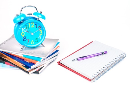 Concept Education or business :  Blue alarm clock is placed on a pile of books with a notebook and...