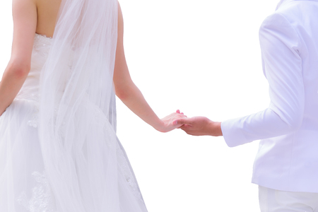 Asian bride in white wedding dress and groom in white suit holding hands isolated on white backgroundの写真素材