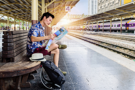Concept life style travel or journey : Young asian Man Traveler Looking at the map while waiting for the train arrives at the station.の写真素材