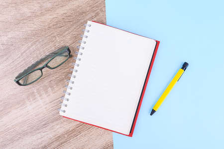 Concept Education or business : The glasses with notebook and yellow pen put on wooden table and blue pastel background.の写真素材