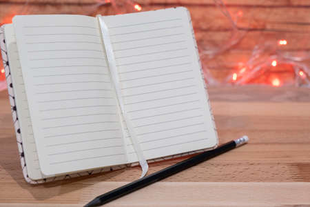 Notebook and pencil on wooden table on background christmas garland.