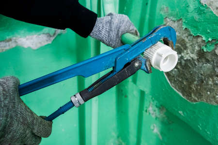 Plumber in grey gloves fastens plastic to steel pipe coupling pipe wrench. The pipe wrench holds the...