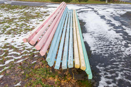 Street bench from multi-colored boards on the background of green grass and white snow.の写真素材