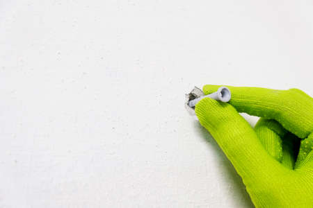 Worker green gloved hand holding putting on facade white plastic screw anchor dowel for building...
