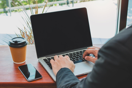 Businessman typing on laptop with smartphone and coffee cup in home office or coffee shopの写真素材