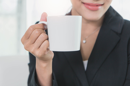 Beautiful young business woman with smile holding white coffee cupの写真素材