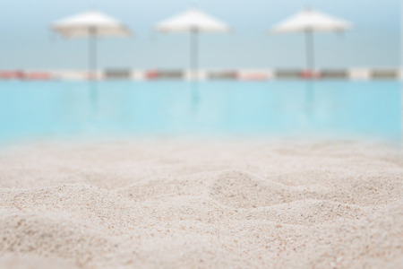 White sand on the beach with blurred swimming pool with benches and umbrella beach on sea background - can used for display or montage your products.の写真素材