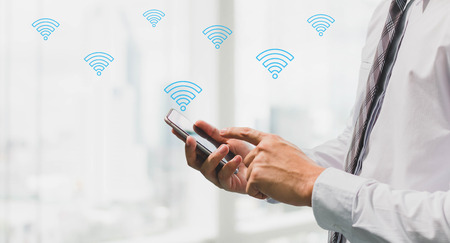 Businessman using smart phone with wifi icon on blurred interior office space background.