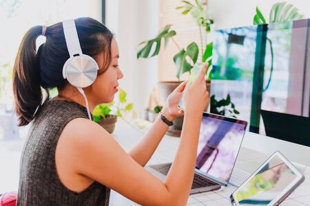 Asian business woman work from home with laptop, tablet and computer on table with headphone.Concept of social distancing is infection control action to stop the spread disease of Corona virus.の写真素材