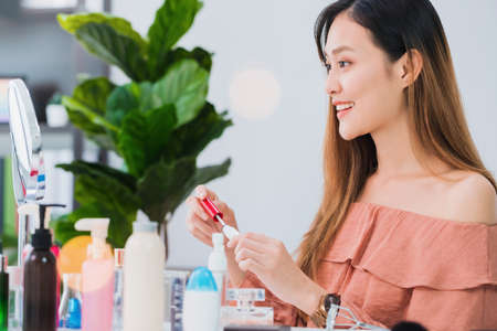 Beautiful asian woman blogger is showing how to make up and use cosmetics in front of the mirror and recording vlog video live streaming at home.Skincare for healthy face concept.の写真素材