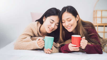 Young beautiful Asian women lesbian couple lover holding coffee cup in bed room at home with smiling...