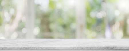 Empty white stone marble table top and blurred of interior restaurant with window view green from...