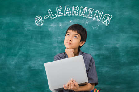 Asian happy school boy thinking and holding laptop on black board with e-learning text...