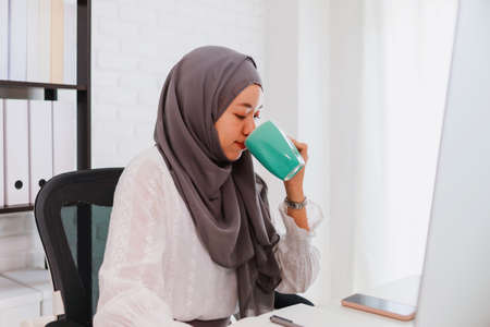 Asian muslim woman student or businesswoman waring hijab.Working from home with computer and drinking coffee.Concept of social distancing working alone at home in the epidemic situation of covid-19.の写真素材