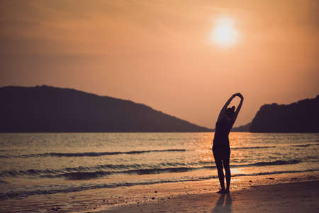 Asian women play yoga on a sand beach by the sea and mountain background in the sunrise morning. Exercise and meditation concept.の写真素材