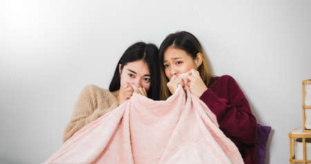 Young beautiful Asian women lesbian couple lover watching horror movie on television on bed  together in bed room at home with fearful face.Concept of LGBT sexuality with happy lifestyle together.の写真素材