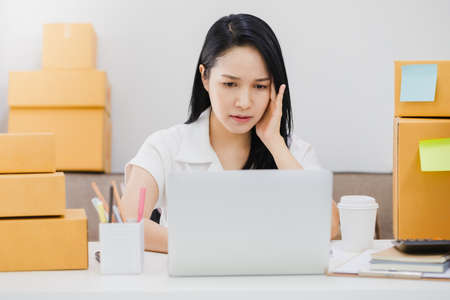Asian beautiful young businesswoman feeling headache and stress in office space background with product box.Concept of Healthcare and Office syndrome.の写真素材