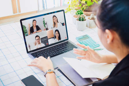 Asian business woman work from home with laptop and computer on table with meeting online and video conferencing.Concept of social distancing to stop the spread disease of Corona virus.の写真素材
