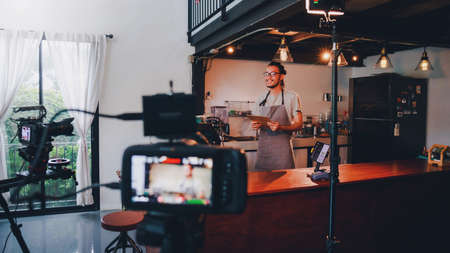 Asian barista man standing in front of the camera and recording vlog video live streaming at bar...