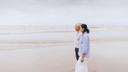 Asian old senior couples walking at the beach by the sea background on weekend vacation.Concept of happy living for the elderly.の写真素材