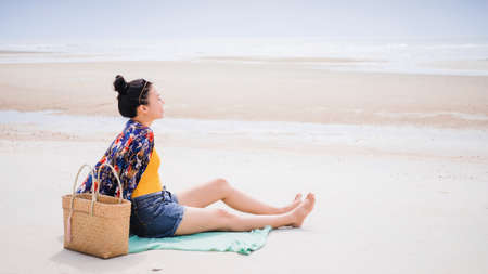 Asian traveller woman sit back and relax on the beach by the sea background on weekend vacation.Concept of happy solo travel.の写真素材