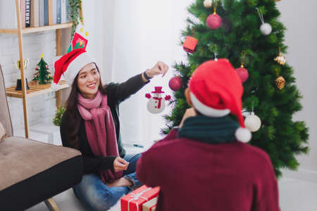 Young Asian couple decorating a Christmas tree in Christmas and Happy New Year holiday festival at home background.Christmas celebration of lover concept.の写真素材
