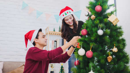 Young Asian couple decorating a Christmas tree in Christmas and Happy New Year holiday festival at home background.Christmas celebration of lover concept.の写真素材