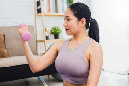 Asian beautiful woman exercise and holding dumbbell at home.Concept of Exercise during the quarantine at home for preventing coronavirus and covid-19 infection.の写真素材