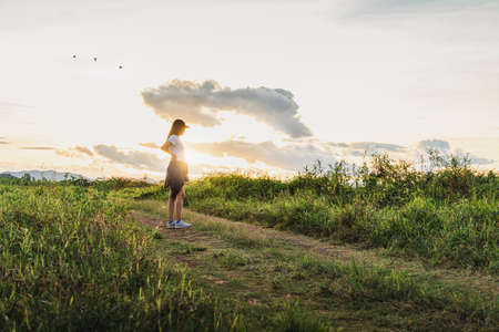 Asian woman standing at grass field with mountain and sunset sky scenic landscape background with copy space.の写真素材