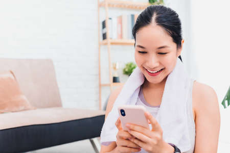 Asian woman using smartphone after play yoga and exercise at home background with copy space.Exercise for Lose weight, increase flexibility And tighten the shape.の写真素材