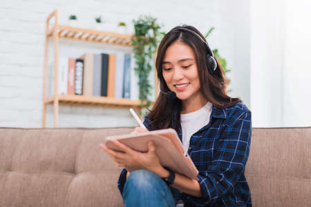 Asian young woman using tablet and headphone working online at living room background.During the...