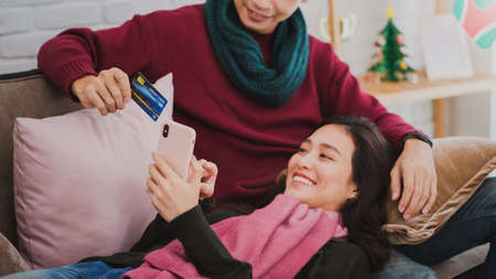 Young Asian couple lover shopping online with credit card and smartphone in room decorated with Christmas trees at home background.Christmas celebration concept.の写真素材