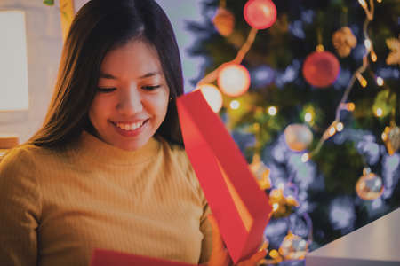 Asian woman open gift box with smiling face at home background with Christmas tree decoration for...