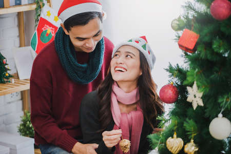 Young Asian couple decorating a Christmas tree in Christmas and Happy New Year holiday festival at home background.Christmas celebration of lover concept.の写真素材