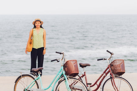 Asian traveler woman traveling with bicycle at beach by the sea background.Concept of a happy summer holiday travel.の写真素材