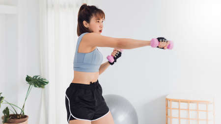 Asian strong woman exercise with dumbbell at home.Concept of Exercise during the quarantine at home