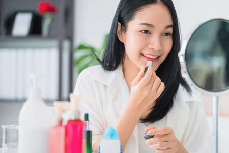 Beautiful asian woman blogger is showing how to make up and use cosmetics. In front of the mirror and smartphone recording vlog video live streaming at home.Skincare for healthy face concept.の写真素材